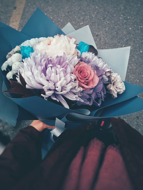 A vibrant floral bouquet featuring large, white and purple chrysanthemums, complemented by a delicate pink rose and smaller purple and white blooms, all arranged in a lush, balanced style. The flowers